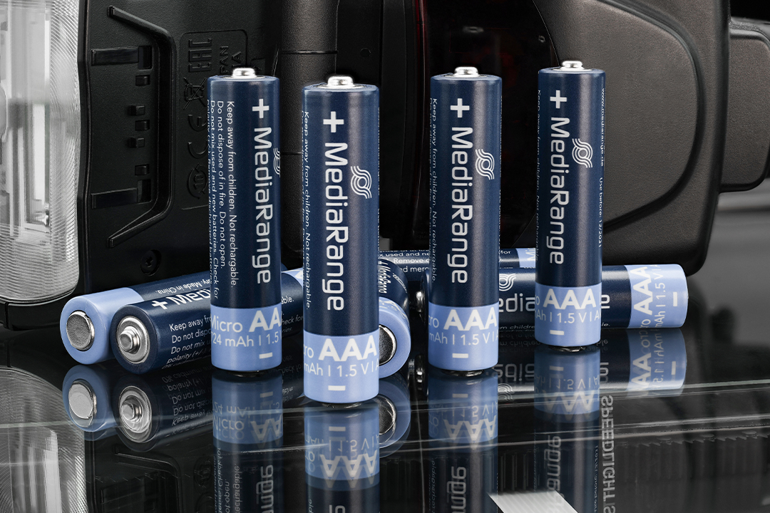 Produktfotografie von MediaRange AAA-Batterien auf einer reflektierenden schwarzen Oberfläche vor einem technischen Gerät.