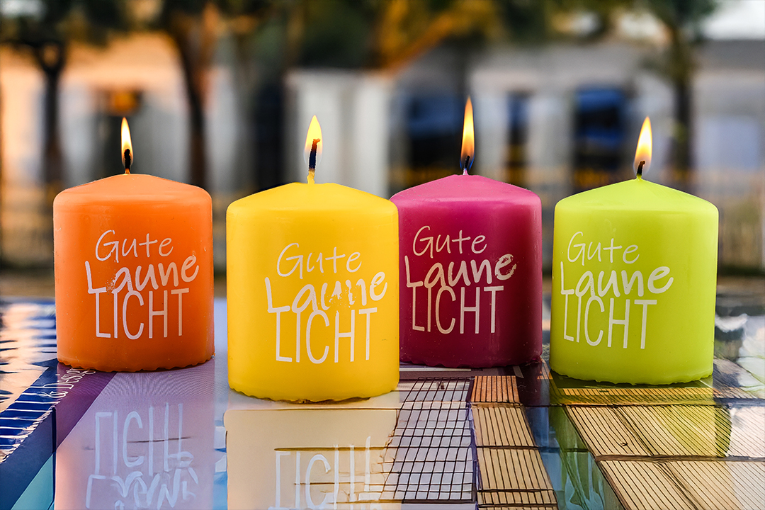 Produktfotografie einer farbigen Kerzenserie mit vier brennenden Gute-Laune-Licht Kerzen und sichtbaren Spiegelungen.