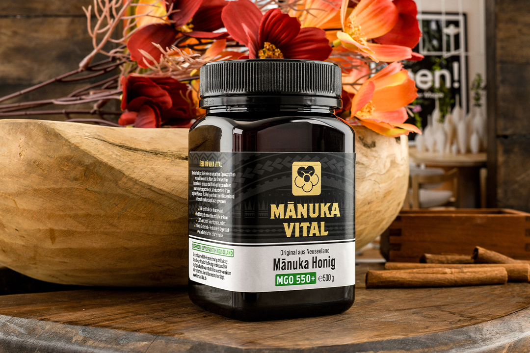 Produktfotografie eines Manuka-Vital-Honigprodukts mit Blumen, Holz und Gewürzen in natürlichem Stillleben