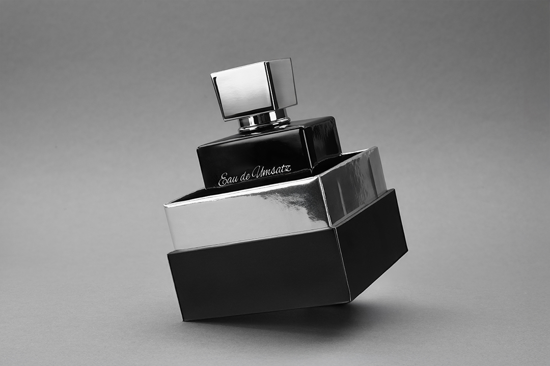 Schwarzer Parfumflakon in geöffneter Verpackung als dynamisch inszenierte Produktaufnahme auf grauem Hintergrund