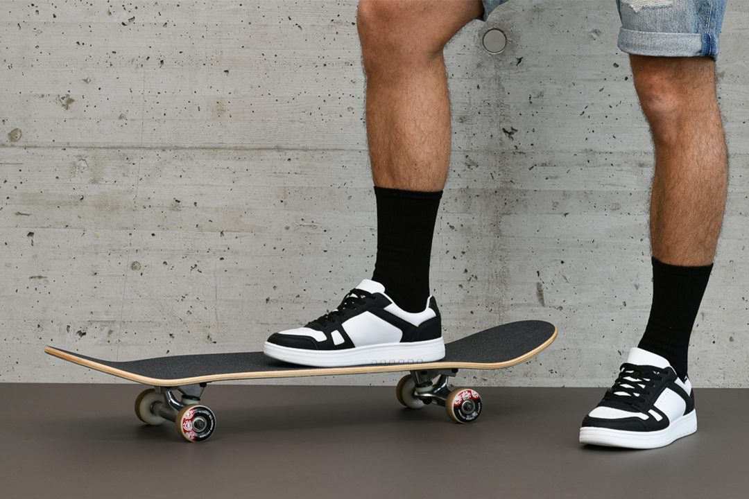 Produktfotografie schwarz-weißer Sneakers an einem Skateboardfahrer vor einer Betonwand.