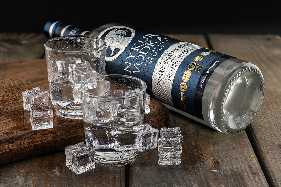Werbefotografie einer Whiskyflasche mit Gläsern und Eiswürfeln als inszeniertes Produktstillleben auf Holzfläche